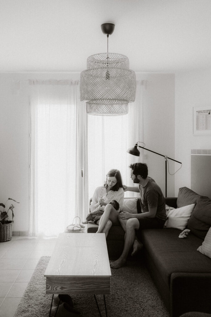 photo en noir et blanc de jeunes parents dans leur salon regardant leur bébé pendant une séance photo avec un photographe à Bordeaux