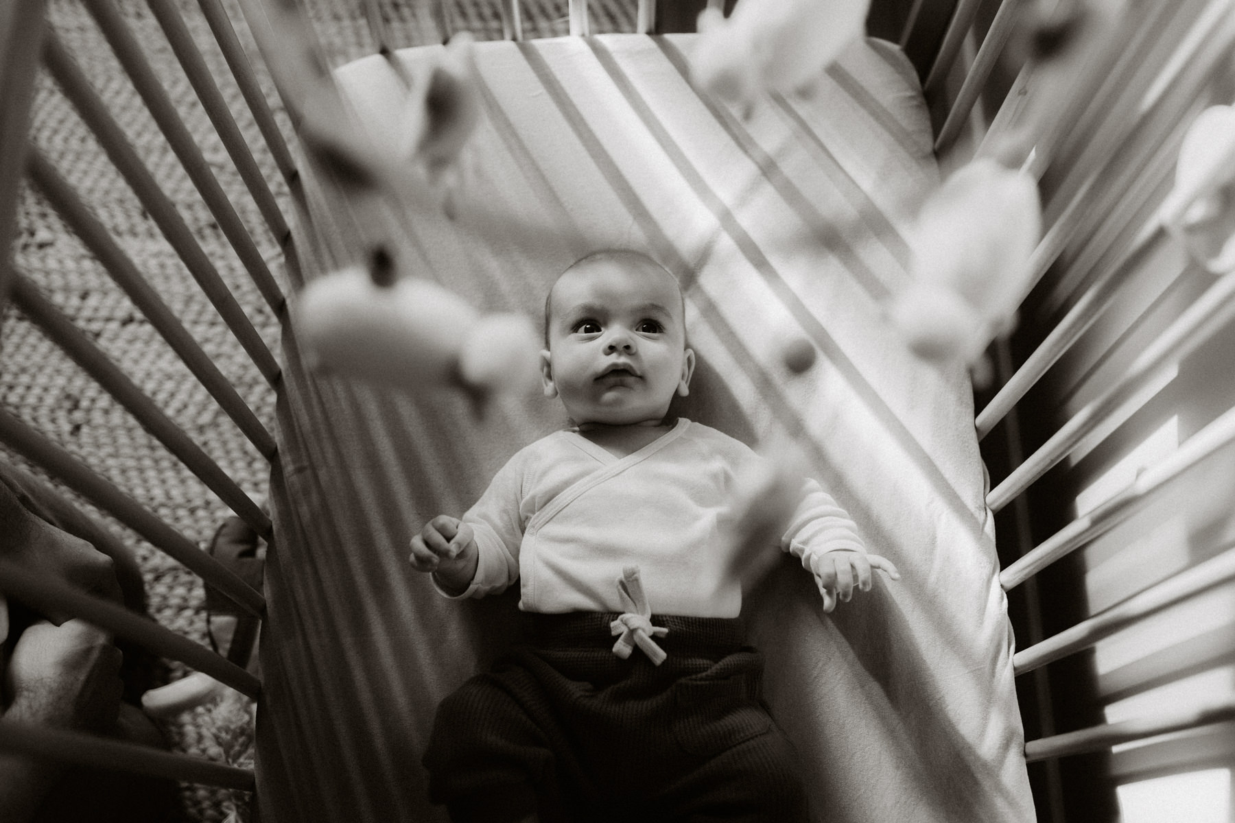 photo de bébé dans son berceau en noir et blanc qui regarde le mobile - photographe bebe à