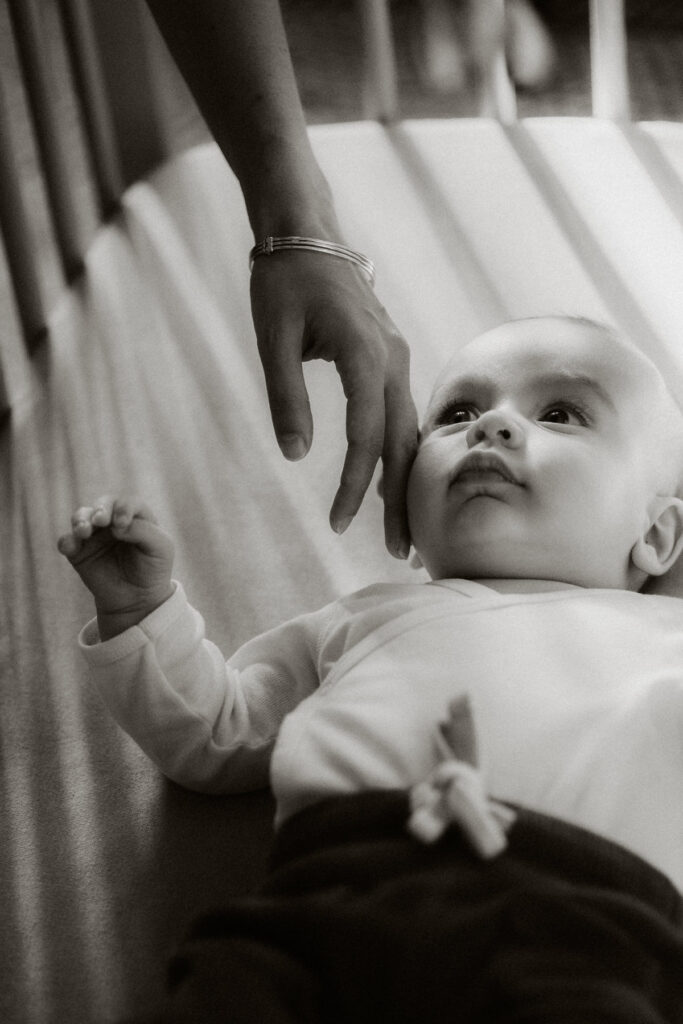bébé dans son berceau avec maman qui lui caresse la joue. photo en noir et blanc photographe bebe bordeaux