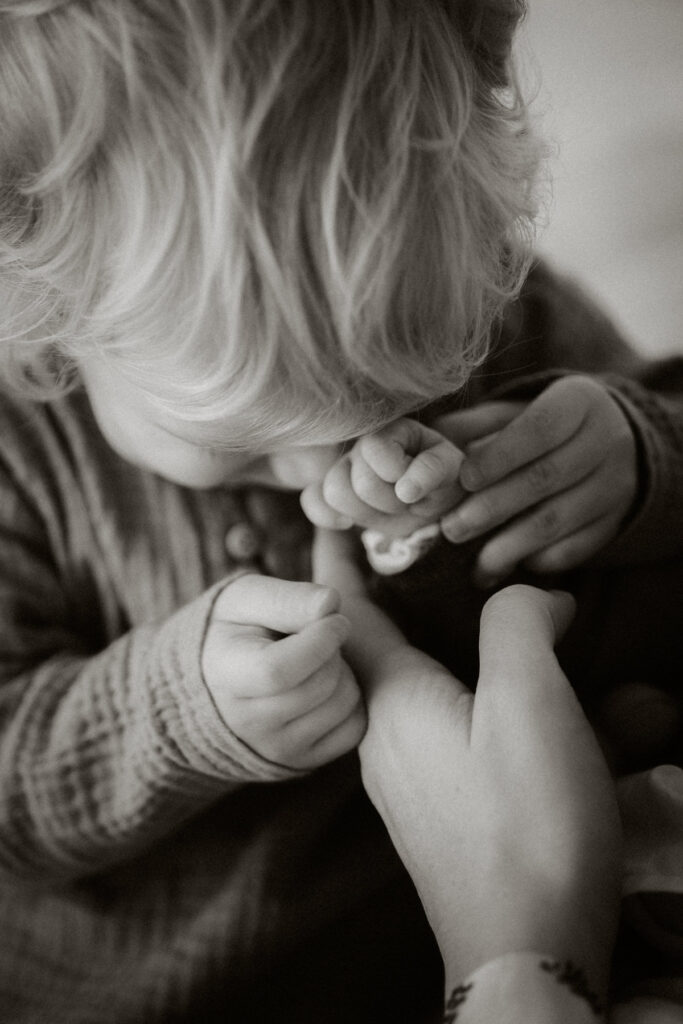 Jeune enfant serrant la main de sa petite soeur - photo en noir et blanc séance nouveau né et famille à Bordeaux