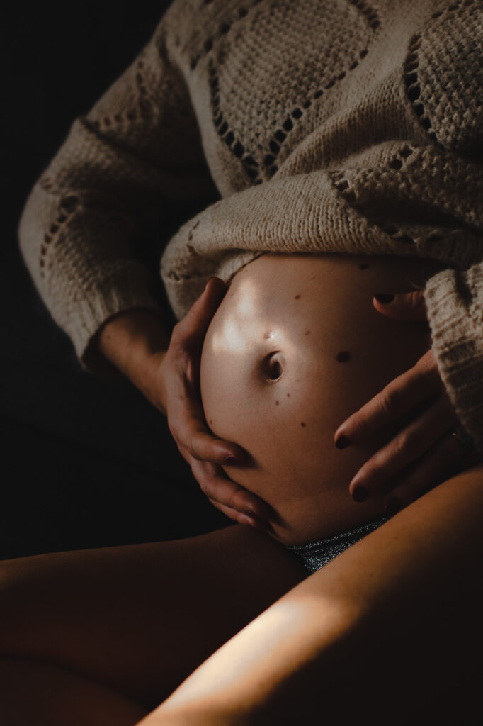photo contrastée d'un ventre rond d'une femme enceinte avec des tâches de lumières à bordeaux
